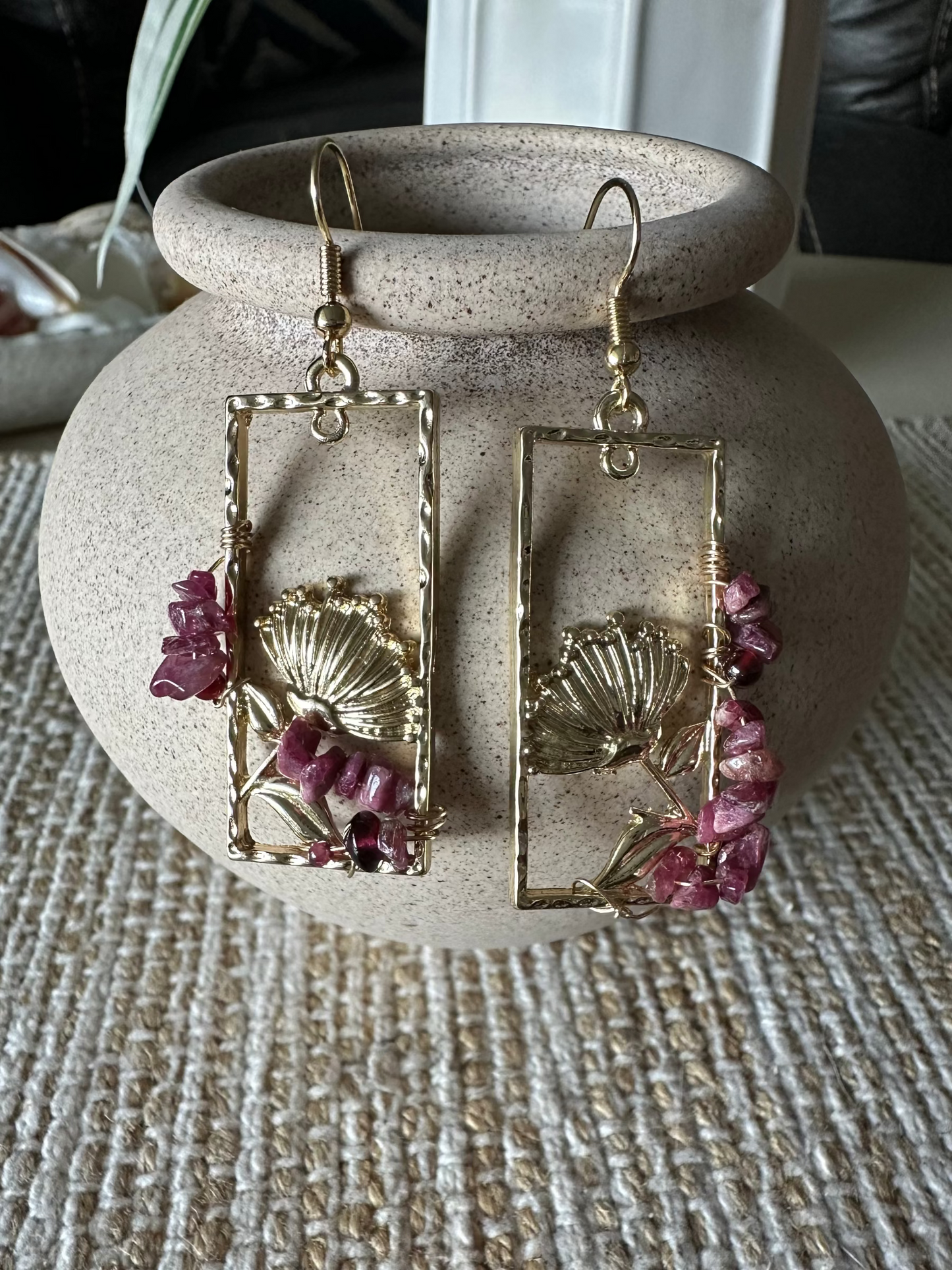 Pair of gold earrings with pink stones on a textured surface