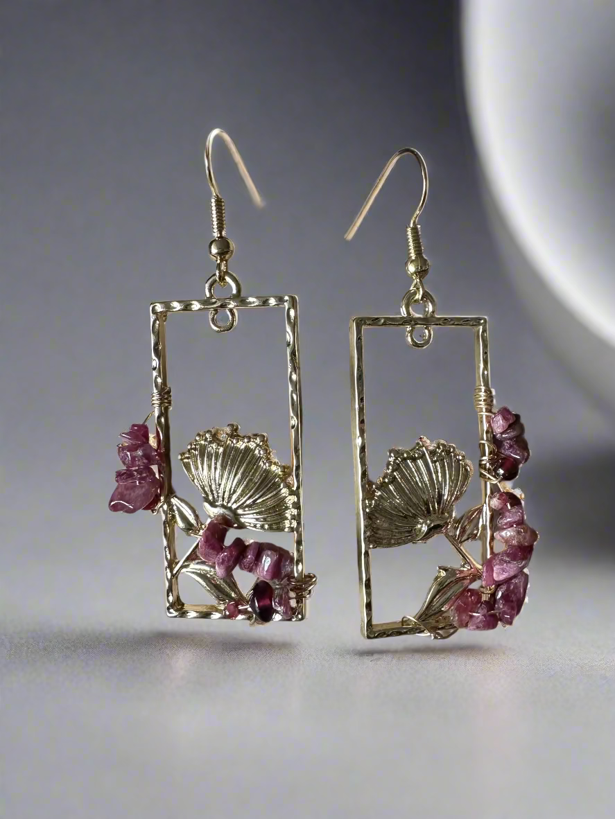Pair of gold earrings with pink gemstones on a textured surface