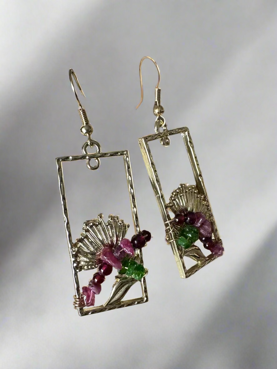 Pair of earrings with rectangular designs and embedded stones on a textured surface.